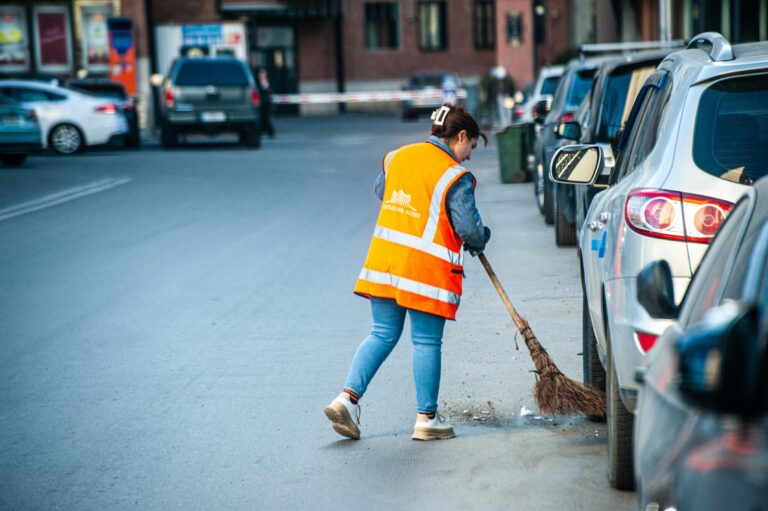A street cleaner in Tbilisi wearing a reflective vest sweeps debris from the roadside.